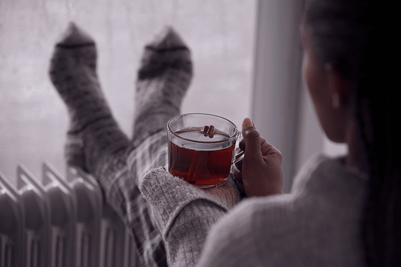 woman sitting near her furnace drinking tea.