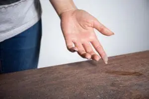 How to Reduce Dust in Your Home. Image is a photograph of a persons hand face up above a dusty table with dust on the pad of their pointer finger.