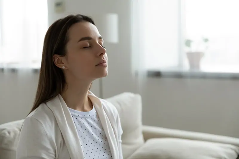 Blogs - Just Right Why Do I Need a Humidifier? Woman sitting on couch with eyes closed.