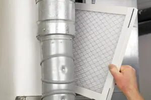 Furnace Filters 101. Male arm and hand replacing disposable air filter in residential air furnace.