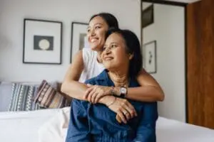 a smiling Asian female embracing her mother and enjoying healthy indoor air quality while they are looking away.