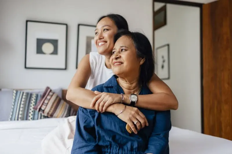 a smiling Asian female embracing her mother and enjoying healthy indoor air quality while they are looking away.