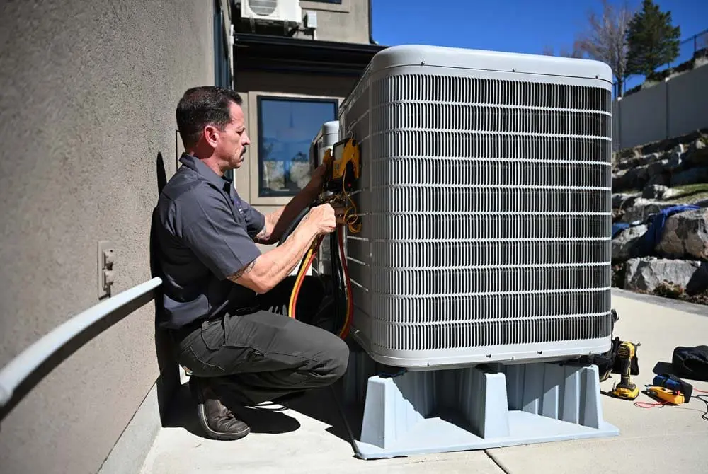 AC Maintenance American Fork UT service from Just Right Plumbing, Heating & Cooling shows an HVAC technician servicing a large outdoor condenser unit beside a residential home. The image includes HVAC gauges, colored service hoses, hand tools, and a technician performing cooling system maintenance on a concrete service area.
