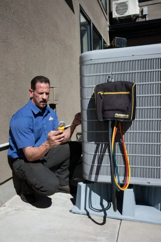 HVAC technician performing AC services in Alpine UT beside an outdoor residential air conditioning condenser unit during a cooling system inspection. The image shows the technician using HVAC diagnostic tools and refrigerant testing equipment while completing air conditioning maintenance and service work. Just Right Plumbing, Heating & Cooling provides AC services, cooling system inspections, and residential HVAC repairs for homeowners in Alpine, Utah. Customers searching for AC services in Alpine UT can contact Just Right Plumbing, Heating & Cooling at (801) 302-1154 for air conditioning repair, seasonal tune-ups, and cooling system diagnostics.