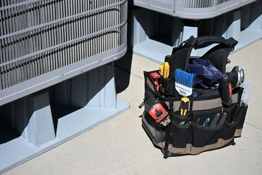 HVAC service tools and repair equipment placed beside outdoor air conditioning condenser units during AC services in American Fork UT. The image shows a technician tool bag filled with HVAC maintenance tools, gauges, measuring devices, and repair equipment used for residential cooling system service. Just Right Plumbing, Heating & Cooling provides AC services, cooling system maintenance, and air conditioning repair for homeowners in American Fork, Utah.