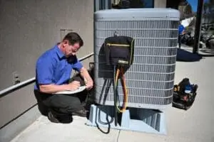 Understanding SEER2 Ratings Before Buying a New HVAC Unit in Utah - Just Right HVAC technician performing AC services in Bountiful UT while completing cooling system inspection paperwork beside an outdoor air conditioning condenser unit. The image shows a residential HVAC service appointment with refrigerant hoses, diagnostic equipment, and service tools connected to the condenser during maintenance work. Just Right Plumbing, Heating & Cooling provides AC services, cooling system inspections, and residential HVAC repairs for homeowners in Bountiful, Utah.