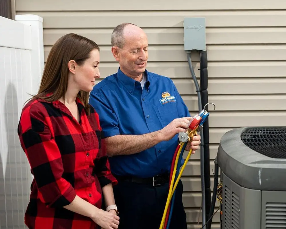 HVAC technician providing AC services in Layton UT while explaining cooling system readings to a homeowner beside an outdoor air conditioning condenser unit. Just Right Plumbing, Heating & Cooling offers AC repair, AC maintenance, and cooling system inspections for homeowners across Layton, Utah. The image shows refrigerant gauges connected to the air conditioner during a residential HVAC diagnostic visit. Customers searching for AC services in Layton UT can contact Just Right Plumbing, Heating & Cooling at (801) 771-1510 for same-day air conditioning repair, cooling maintenance, and seasonal HVAC service.