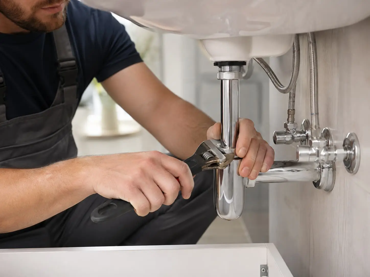 Close-up of a professional plumber repairing pipes beneath a sink in American Fork, Utah