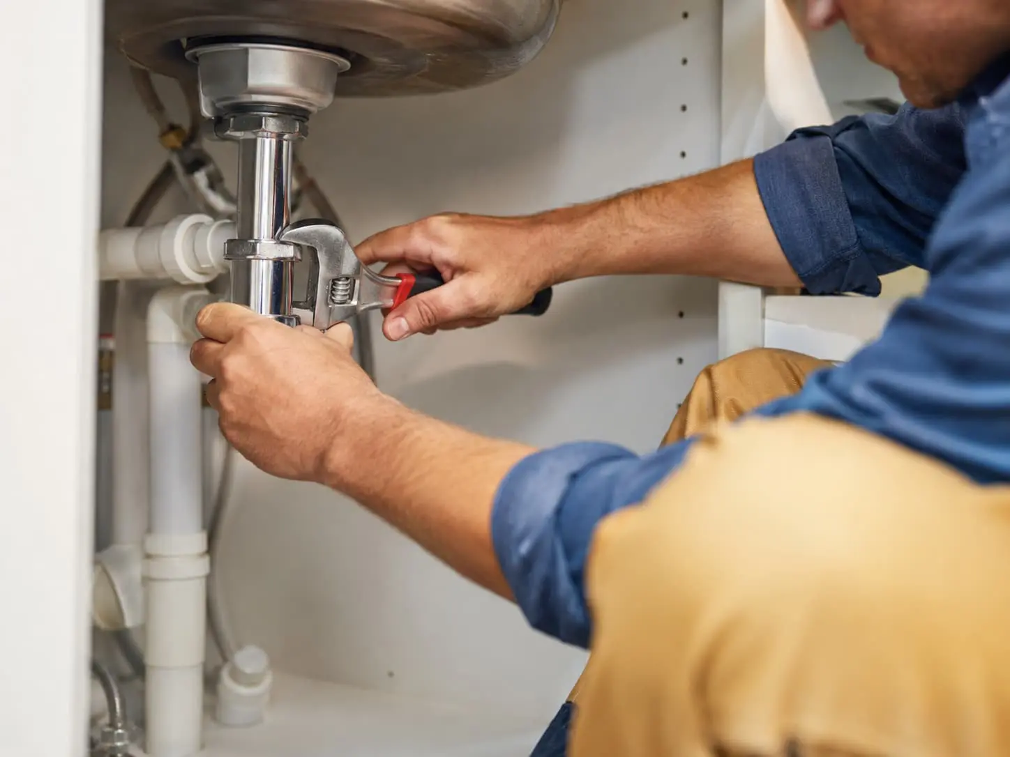 Plumber repairing pipes under a sink in Layton, UT