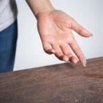 How to Reduce Dust in Your Home. Image is a photograph of a persons hand face up above a dusty table with dust on the pad of their pointer finger.