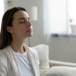 Why Do I Need a Humidifier? Woman sitting on couch with eyes closed.