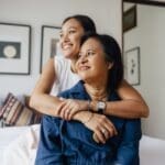 a smiling Asian female embracing her mother and enjoying healthy indoor air quality while they are looking away.