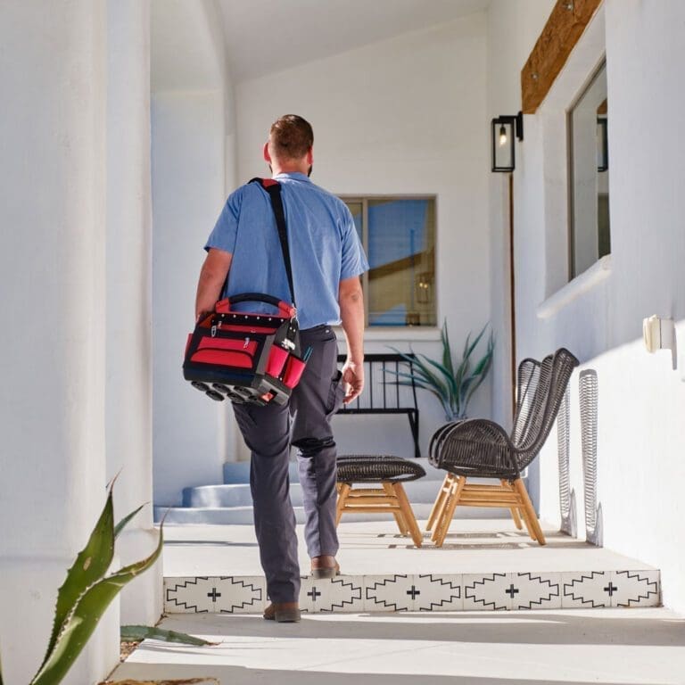 AC Maintenance Alpine UT service from Just Right Plumbing, Heating & Cooling shows an HVAC technician arriving at a residential property carrying a service tool bag for a scheduled cooling system visit. The image includes a bright home entryway with outdoor seating, tiled steps, and a technician preparing to inspect or maintain the air conditioning system. Just Right Plumbing, Heating & Cooling provides AC maintenance, cooling inspections, and seasonal HVAC service for homeowners in Alpine, UT. Call (801) 302-1154 for AC Maintenance Alpine UT service from a local HVAC team.