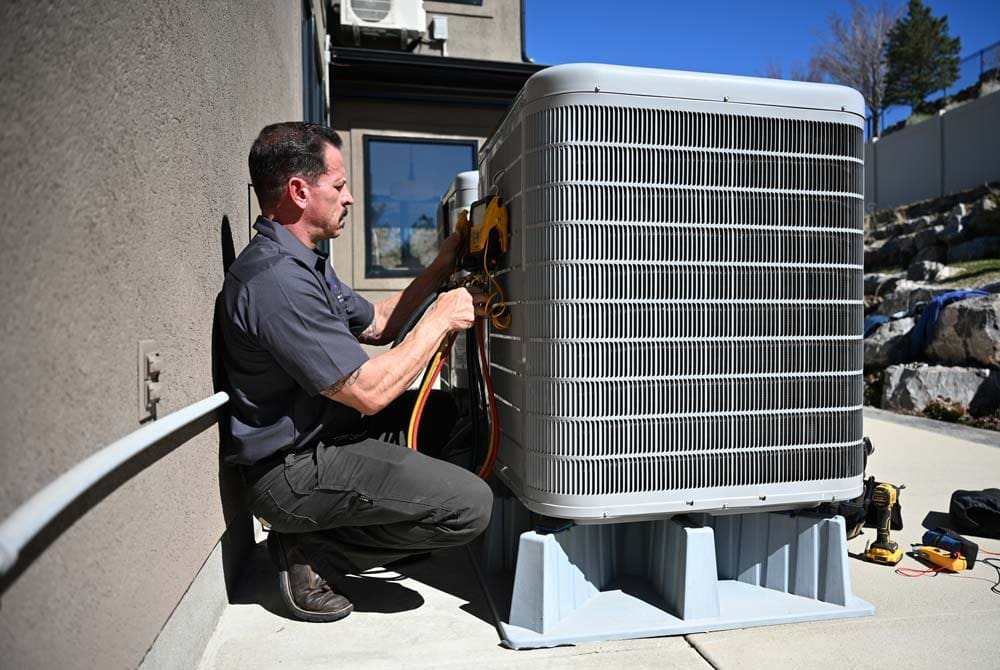 AC Maintenance American Fork UT service from Just Right Plumbing, Heating & Cooling shows an HVAC technician servicing a large outdoor condenser unit beside a residential home. The image includes HVAC gauges, colored service hoses, hand tools, and a technician performing cooling system maintenance on a concrete service area.
