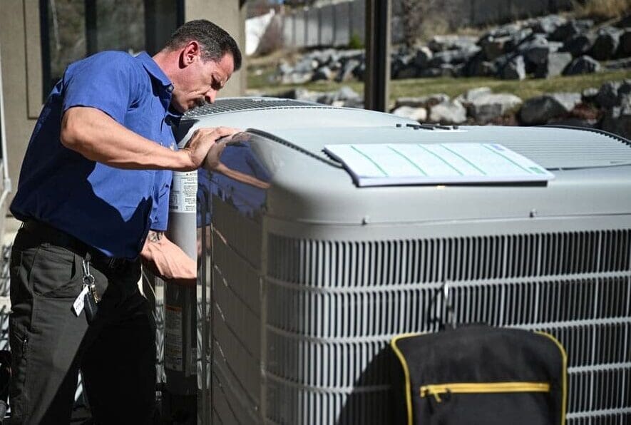 HVAC technician performing AC maintenance in Layton UT while inspecting outdoor air conditioning condenser units during a residential cooling system service appointment. The image shows a technician working directly on the condenser system with HVAC tools beside multiple AC units near a home exterior. Just Right Plumbing, Heating & Cooling provides AC maintenance, cooling system inspections, and seasonal air conditioning service for homeowners in Layton, Utah. Customers needing AC maintenance in Layton UT can contact Just Right Plumbing, Heating & Cooling at (801) 771-1510 for cooling tune-ups, condenser inspections, and residential HVAC service.