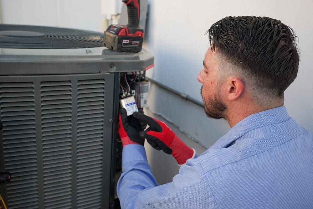 HVAC technician performing AC maintenance in South Salt Lake UT while inspecting and replacing electrical components inside an outdoor residential air conditioning condenser unit. The image shows cooling system maintenance work involving HVAC wiring, capacitor inspection, and professional repair tools during a residential service appointment. Just Right Plumbing, Heating & Cooling provides AC maintenance, cooling system diagnostics, and residential HVAC tune-ups for homeowners in South Salt Lake, Utah.