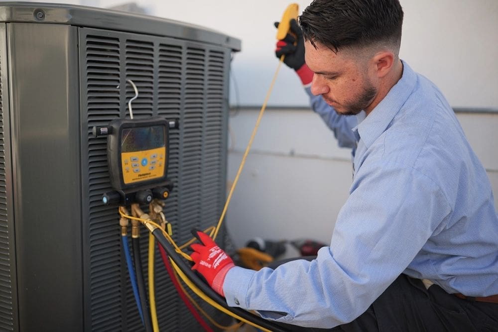 HVAC technician performing AC services in Alpine UT while testing an outdoor air conditioning condenser with digital refrigerant gauges and HVAC hoses. The image shows a residential cooling system inspection during an air conditioning maintenance and diagnostic service appointment. Just Right Plumbing, Heating & Cooling provides AC services, cooling system repairs, and seasonal HVAC maintenance for homeowners in Alpine, Utah. Customers needing AC services in Alpine UT can contact Just Right Plumbing, Heating & Cooling at (801) 302-1154 for air conditioning repair, cooling diagnostics, and residential HVAC inspections.
