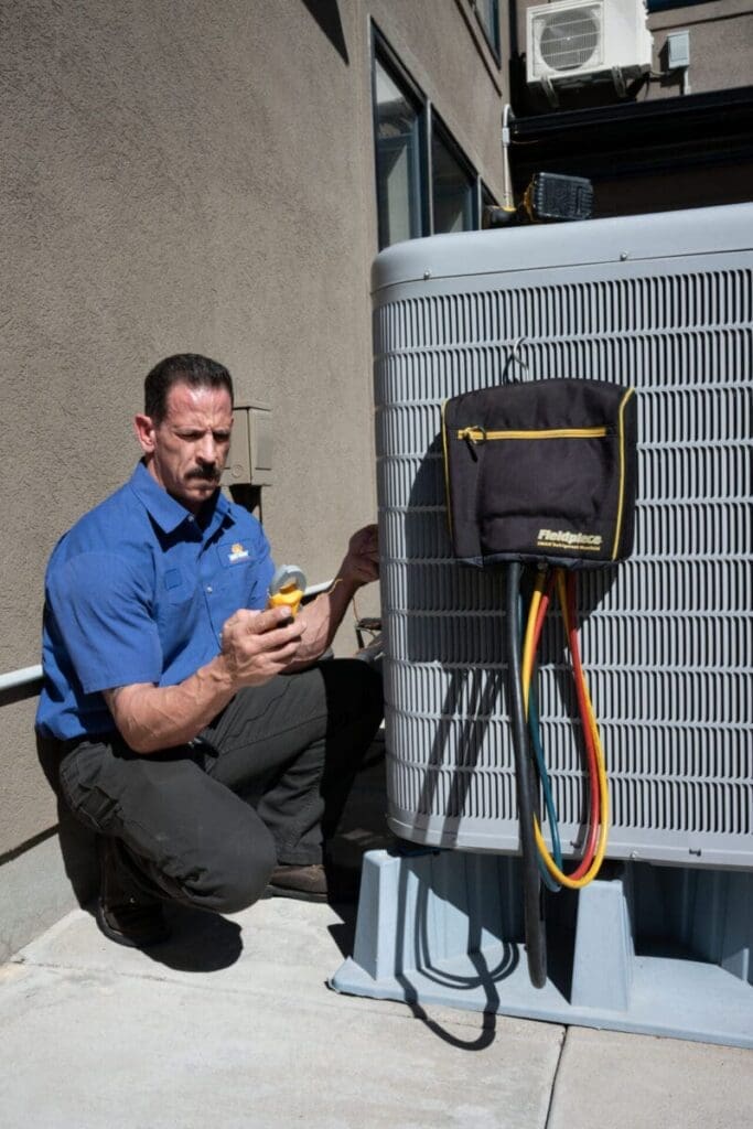 HVAC technician performing AC services in Alpine UT beside an outdoor residential air conditioning condenser unit during a cooling system inspection. The image shows the technician using HVAC diagnostic tools and refrigerant testing equipment while completing air conditioning maintenance and service work. Just Right Plumbing, Heating & Cooling provides AC services, cooling system inspections, and residential HVAC repairs for homeowners in Alpine, Utah. Customers searching for AC services in Alpine UT can contact Just Right Plumbing, Heating & Cooling at (801) 302-1154 for air conditioning repair, seasonal tune-ups, and cooling system diagnostics.