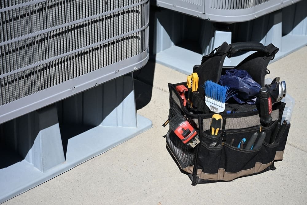 HVAC service tools and repair equipment placed beside outdoor air conditioning condenser units during AC services in American Fork UT. The image shows a technician tool bag filled with HVAC maintenance tools, gauges, measuring devices, and repair equipment used for residential cooling system service. Just Right Plumbing, Heating & Cooling provides AC services, cooling system maintenance, and air conditioning repair for homeowners in American Fork, Utah.