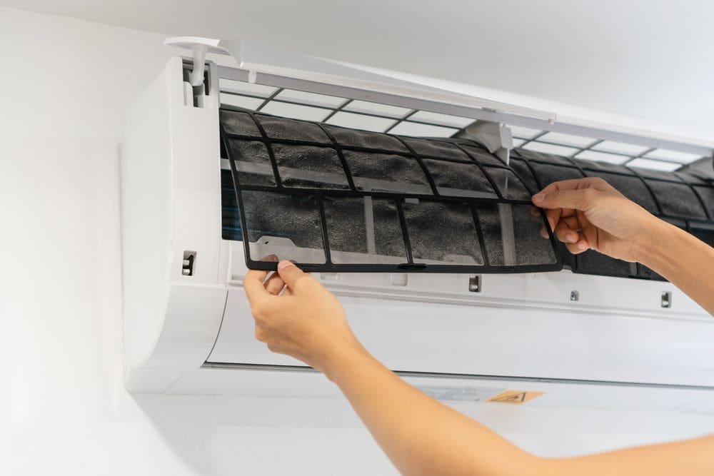 Technician removing and cleaning a ductless mini split AC filter during AC services in American Fork UT inside a residential home. The image shows a dirty air filter being removed from a wall-mounted mini split air conditioning system during routine HVAC maintenance. Just Right Plumbing, Heating & Cooling provides AC services, mini split maintenance, and indoor cooling system inspections for homeowners in American Fork, Utah.