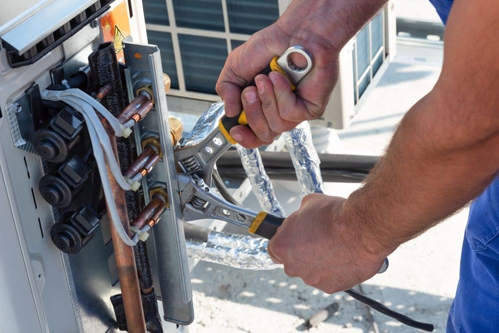 HVAC technician performing AC services in Bluffdale UT while tightening refrigerant line connections on a residential air conditioning system. The image shows close-up HVAC repair work involving copper piping, insulated refrigerant lines, and cooling system maintenance tools during a residential service appointment. Just Right Plumbing, Heating & Cooling provides AC services, cooling system repairs, and residential HVAC maintenance for homeowners in Bluffdale, Utah. The visible refrigerant lines, copper fittings, and service tools reflect real residential AC repair work completed during professional cooling system maintenance visits.