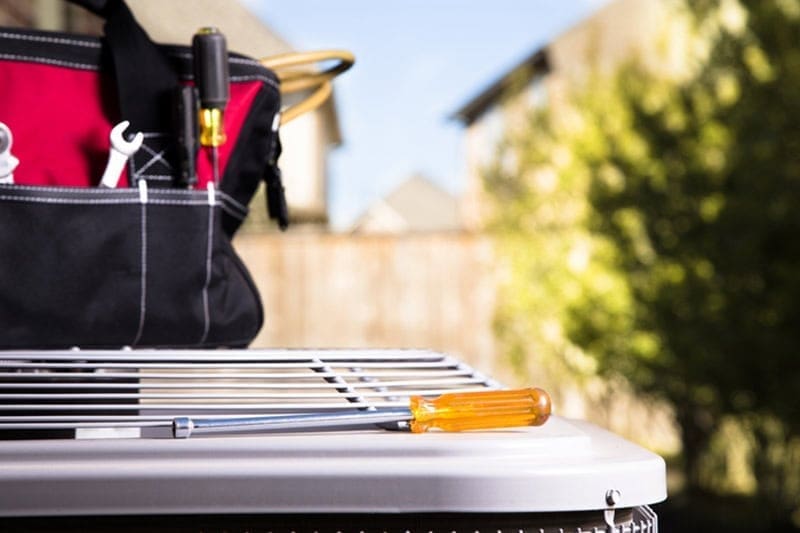 HVAC service tools and repair equipment placed on top of an outdoor air conditioning condenser during AC services in Bluffdale UT. The image shows screwdrivers, a technician tool bag, and residential cooling system equipment prepared for HVAC maintenance and repair work. Just Right Plumbing, Heating & Cooling provides AC services, cooling system maintenance, and air conditioning repair for homeowners in Bluffdale, Utah. The visible condenser unit, HVAC tools, and outdoor residential setting reflect real equipment used during professional air conditioning maintenance visits.