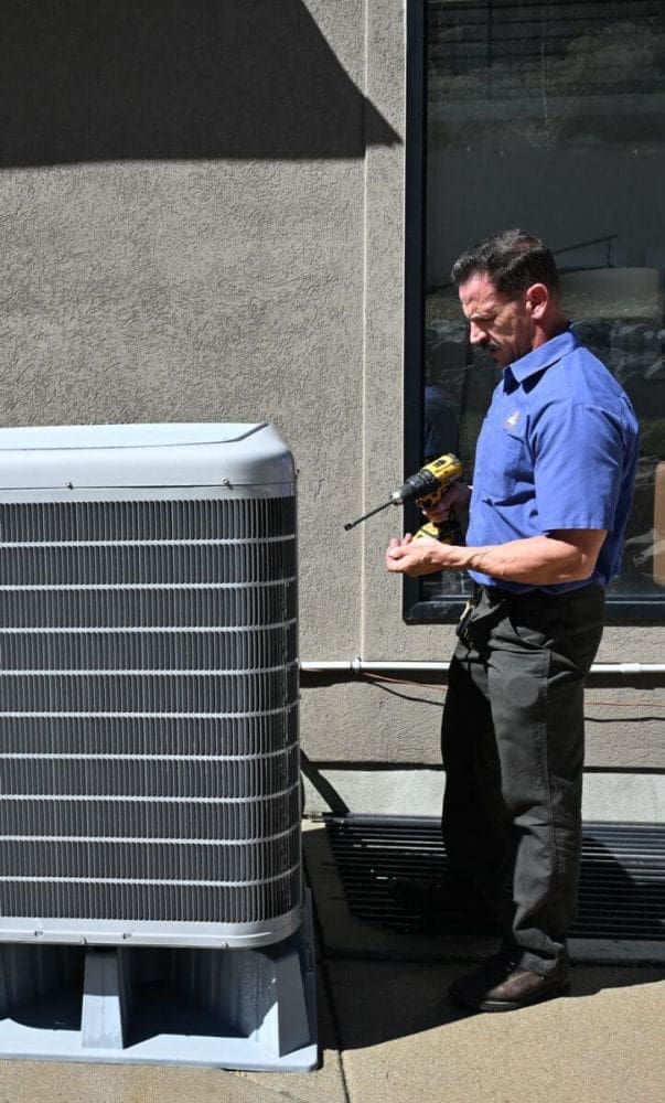 HVAC technician performing AC services in Layton UT beside an outdoor air conditioning condenser unit during a residential cooling system maintenance visit. The image shows a service technician holding repair tools while inspecting an exterior AC system near a home. Just Right Plumbing, Heating & Cooling provides air conditioning repair, AC maintenance, and cooling system inspections for homeowners throughout Layton, Utah. Customers needing AC services in Layton UT can call Just Right Plumbing, Heating & Cooling at (801) 771-1510 for same-day cooling repairs, seasonal tune-ups, and HVAC diagnostics.