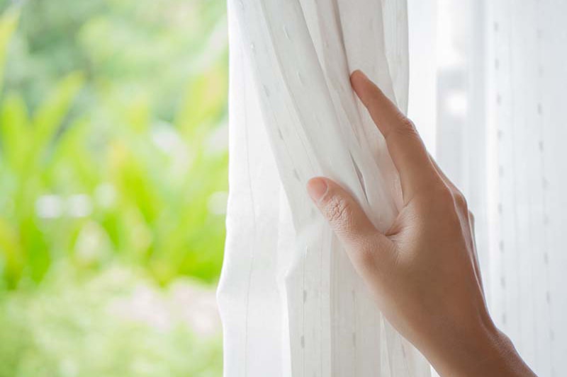Spring Money-Saving Tips. Hand pulling curtain aside in front of window.