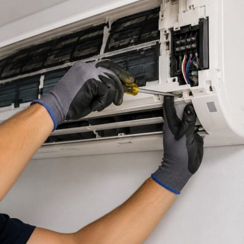 Technician repairing an indoor AC unit in South Salt Lake UT, using a screwdriver on the open wall-mounted air conditioner.