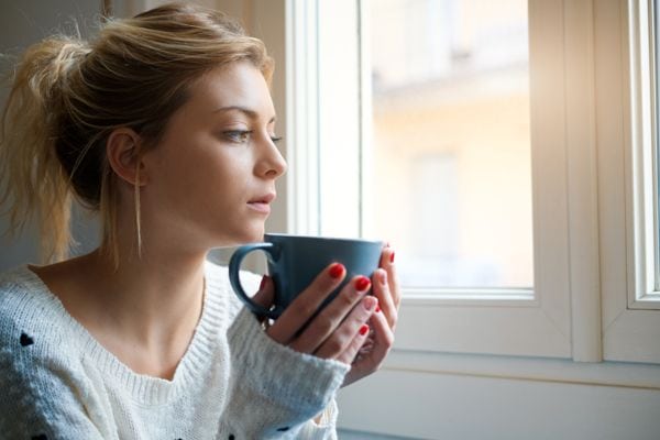 A woman sits by a window with a cup. Should I Get an 80% or 95% Furnace?